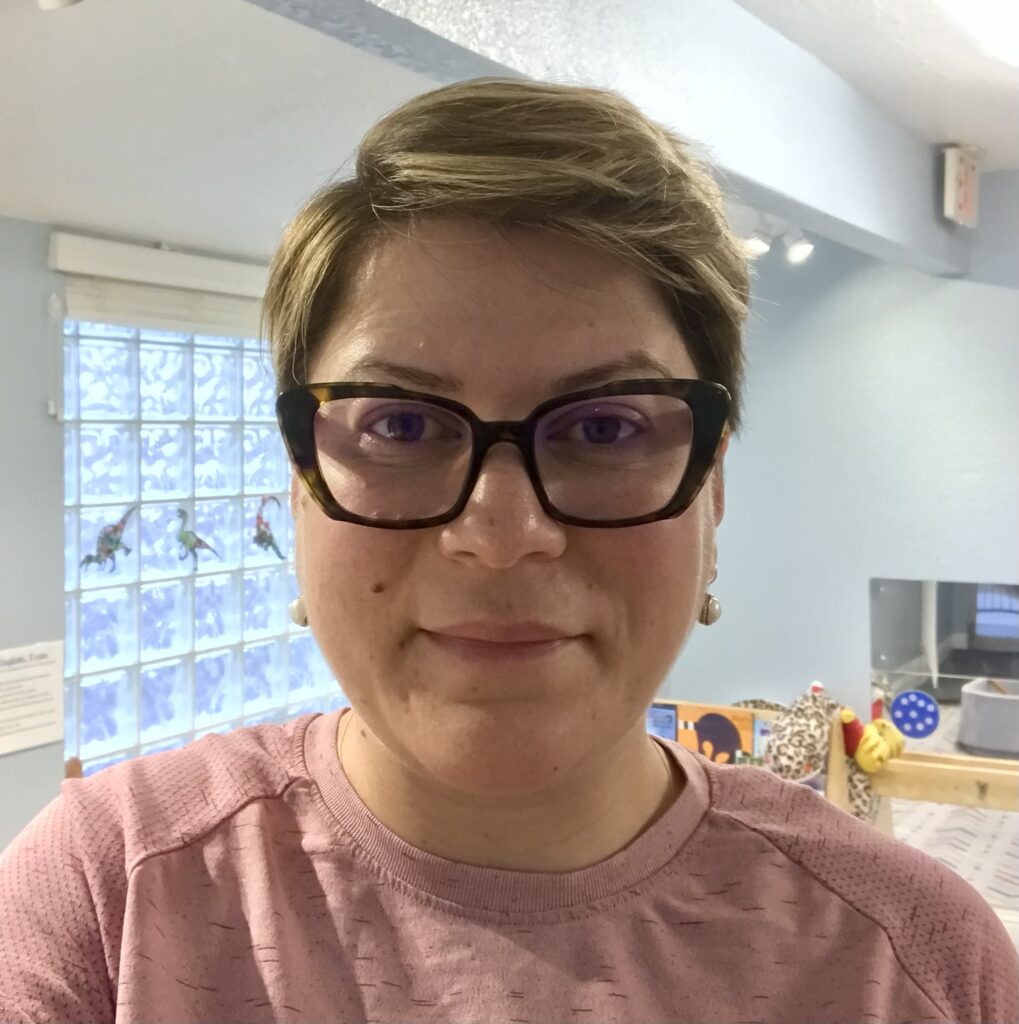 Headshot of Ramella Lee in pink shirt, with dark rimmed glasses, against an office background.