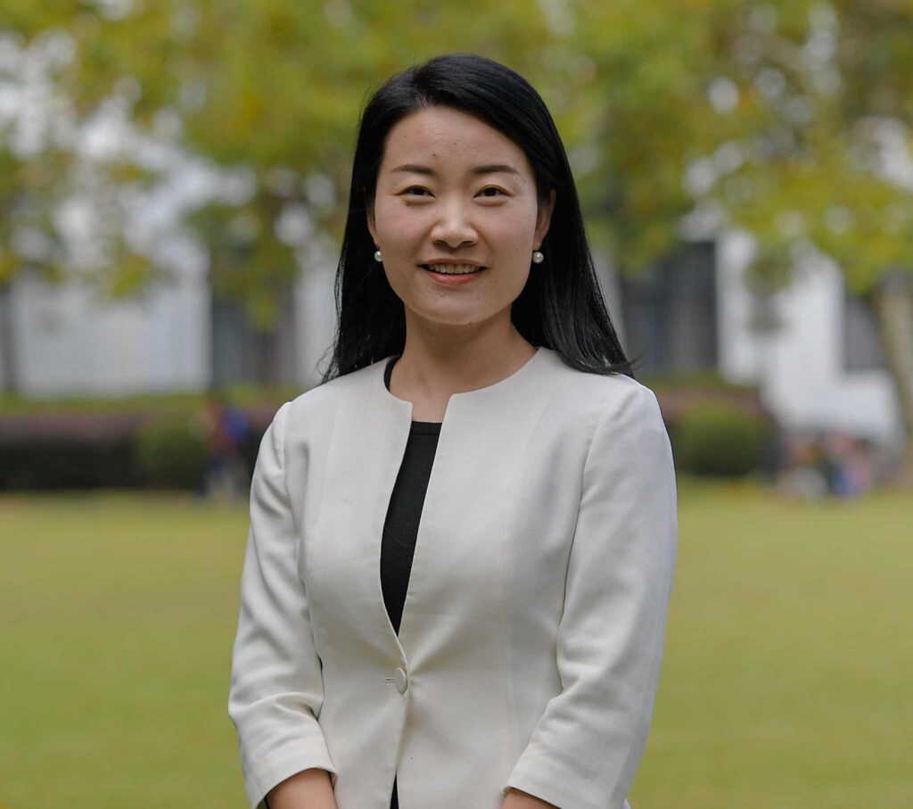 Headshot of Di Liu in a pearl grey blazer against green outdoor.